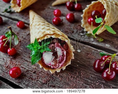 homemade ice cream cherries and chocolate in a waffle cone, fresh cherries on old wooden table - right side view