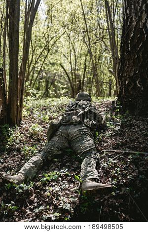 Soldier in military uniform lies in ambush at forest
