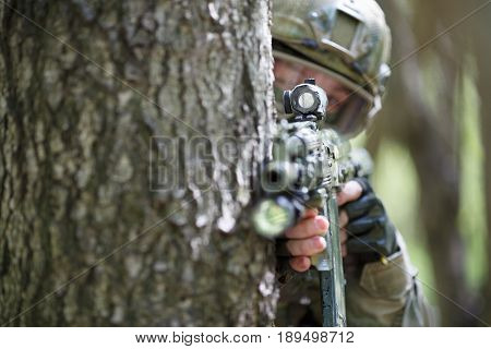 Soldier with rifle peeks out from behind tree in forest
