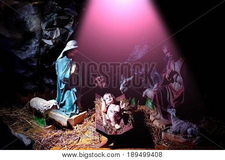 Christmas Infant Jesus lying in manger or crib in rays of divine light with mother Mary Joseph sheep donkey ox in cave. Nativity scene. Holy family. Christianity religion holidays celebration