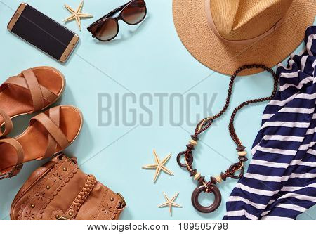 Summer sea background and women's beach accessories: straw hat, bracelets, leather sandals, glasses, beads, leather bag and striped dress, phone samsung 7 Edge. Copy space. Flat lay.