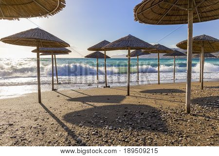 Umbreles on the sand beach with cloudy blue sky, sun and sea waves