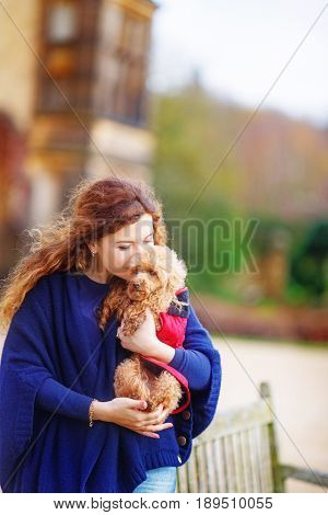 The girl in a blue cape gently hugs her little dog rejoicing at the long-awaited meeting with the pet. She closed her eyes and pressed the poodle to her face