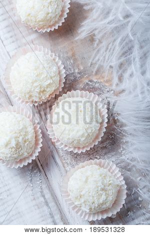 Homemade white truffles candy dessert sprinkled in coconut chips on wooden background close up. Delicious chocolate praline with decor. Top view