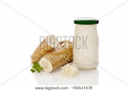 Fresh grated horseradish and root and sauce in glass jar isolated on white background.