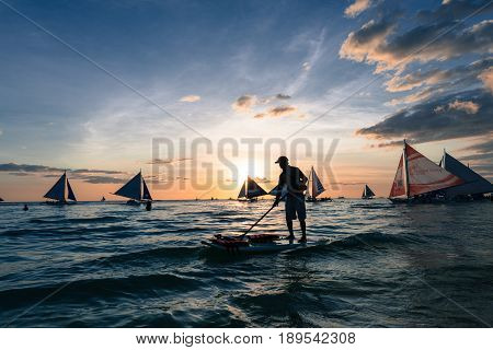 BORACAY, WESTERN VISAYAS, PHILIPPINES - MARCH 24, 2017: Colorful sunset with stand up paddle man full of sailboats