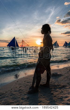 BORACAY, WESTERN VISAYAS, PHILIPPINES - MARCH 24, 2017: Surfer man posing in the colorfukl sunset in White Beach, Boracay.