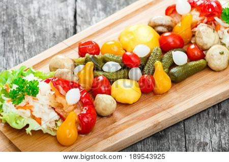 Assorted pickled vegetables - Sauerkraut cabbage peppers cucumbers tomatoes onions mushrooms and herbs on cutting board on wooden background close up. Snacks and Wine appetizers set