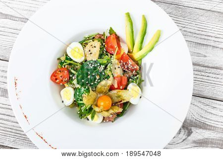 Fresh salad with tuna spinach arugula codfish artichokes quail eggs avocado cherry tomatoes physalis and sesame on wooden background close up. Mediterranean food