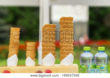 Many empty wafer sweet cornets for ice cream on naturale green blurry background. Selective focus. Copy space. Real scene in the store. Concept of summer, sweets, lifestyle