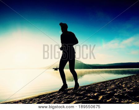 Healthy Lifestyle. Tall Young Man Runner Is Running On Sunrise Seaside. Man Jump In Sand