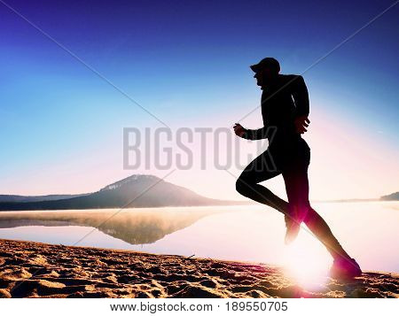 Healthy Lifestyle. Tall Young Man Runner Is Running On Sunrise Seaside. Man Jump In Sand