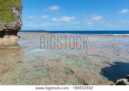Three color areas of red colored mosaic-like pattern coral shelf with turquoise sea and blue sky beyond surounding bottom of tropical atoll island of Niue