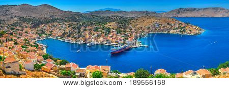 Panoramic view on beautiful Symi island Aegean Sea blue bay Greek houses on green hills, yacht sea port, tourist ferryboat. Famous Mediterranean MSC cruises. Greece islands holiday vacation tours trip