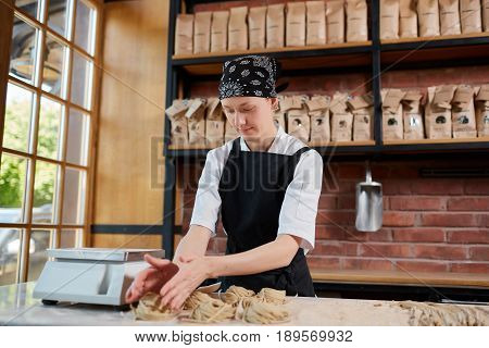 Horizontal indoors shot of female cook forming taglatellepasta in a kitchen of restaurant. Woman forming taglatellein cafe