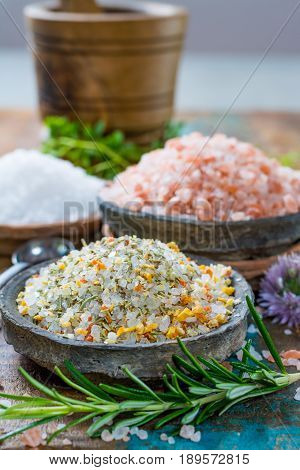 Different types of natural salt in stone bowls on wooden surface. White sea salt pink Himalayan salt Spiced salt with rosemary