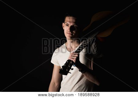 Music and creativity. Handsome young man in a T-shirt and jeans stands with an acoustic guitar on his shoulder on a black isolated background