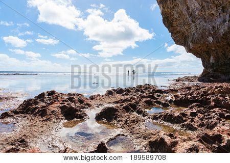 Niue, South Pacific - May 25, 2017;  two people in distance exploring rock pools on coral shelf on tropical Niue