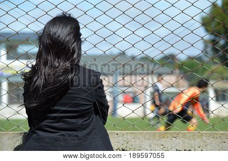 Young mother watches attentively the game of her son soccer player from the edge of the playing field