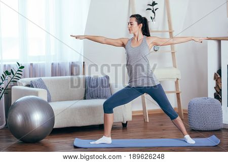 Young cheerful attractive woman practicing yoga at home, working out wearing sportswear, top, pants, indoor full length