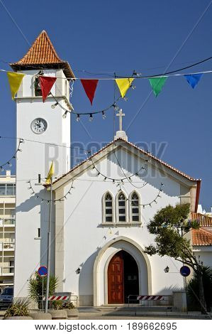 A small white church in Algrave with festive decorations hanging in front of it.