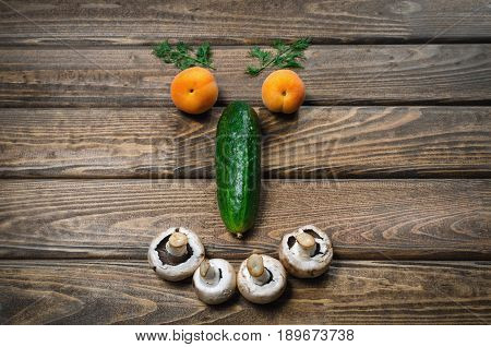 smiling face with vegetables eyebrows with dill apricot eyes cucumber nose and teeth of mushrooms on a wooden table