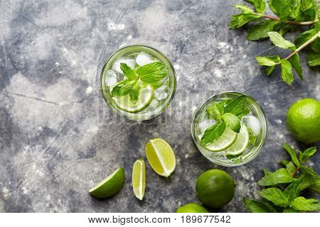 Mojito cocktail alcohol refreshment drink in highball glass, summer tropical vacation beverage with rum, mint leaves, lime citrus juice, soda water and ice on concrete table. Top view