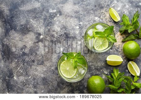 Mojito cocktail alcohol bar drink traditional Cuba beverage top view copy space two highball glass, with rum, citrus slice, mint, lime, soda water and ice on concrete table.