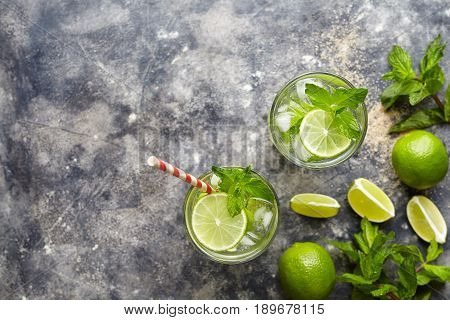 Mojito cocktail alcohol bar drink traditional fresh tropical beverage top view copy space two highball glass, with rum, citrus slice, spearmint, lime juice, soda water and ice on concrete table.