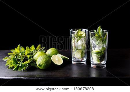 Mojito traditional refreshing cocktail alcohol drink in glass bar preparation with lime, mint leaves, sugar, and rum. Dark black background with copy space for text