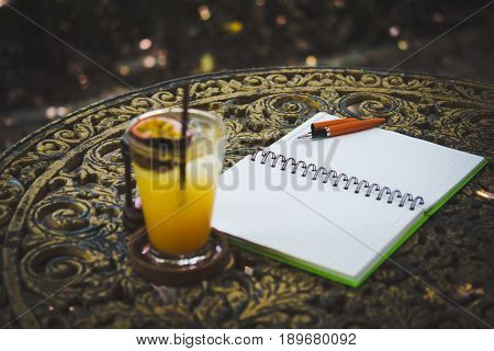 Fresh passion fruit juice in glass on table with is tree garden background notepad and pen