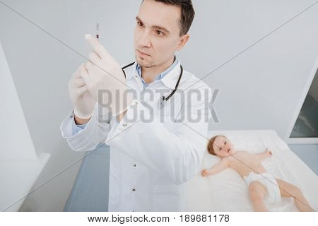 Scrupulous task. Trained neat wise doctor estimating the right dosage and checking a syringe while conducting a regular procedure for toddlers