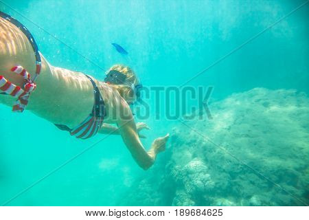 Woman snorkeler swims in tropical sea with american flag bikini. Underwater scene of a female apnea and doing skin diving. Watersport activity in Hawaii. Tropical destination holiday travel.