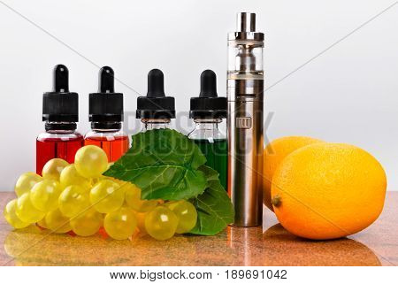 Electronic cigarette bottles with vape liquid lemons and fake bunch of grapes on granite surface and white background