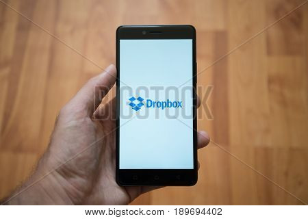 London, United Kingdom, june 5, 2017: Man holding smartphone with Dropbox logo on the screen. Laminate wood background.