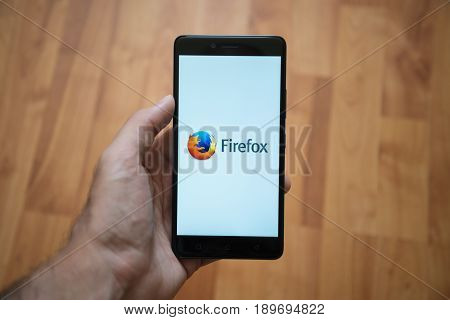 London, United Kingdom, june 5, 2017: Man holding smartphone with Mozilla Firefox logo on the screen. Laminate wood background.