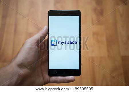 London, United Kingdom, june 5, 2017: Man holding smartphone with Myspace logo on the screen. Laminate wood background.