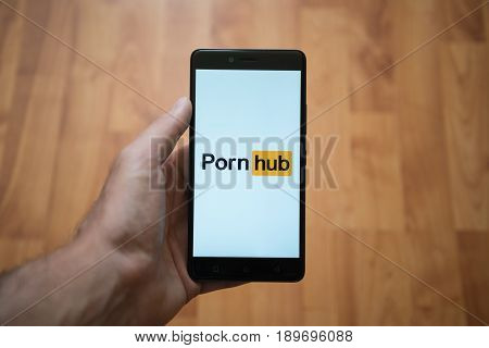 London, United Kingdom, june 5, 2017: Man holding smartphone with Pornhub LOGO on the screen. Laminate wood background.
