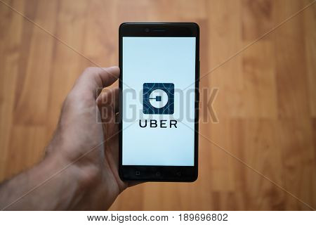 London, United Kingdom, june 5, 2017: Man holding smartphone with Uber LOGO on the screen. Laminate wood background.