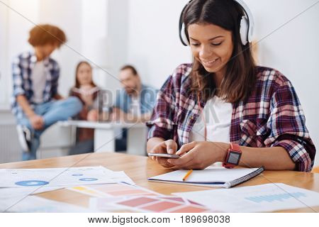 Way of focusing. Smart persistent focused woman wearing headphones and getting ready with her assignment for tomorrows class while looking for inspirational song to start with