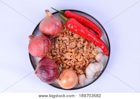 Dried shrimp, fresh Bombay onions, fresh red chilies, fresh shallots, fresh garlics on a white ceramic plate with blue outer ring line.  White background.