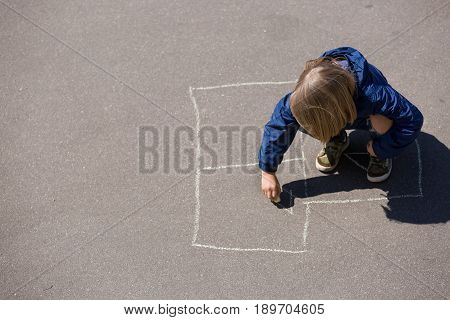 Kid boy drawing hopscotch on asphalt. Child playing hopscotch on playground outdoors on a sunny day. outdoor activities for children.