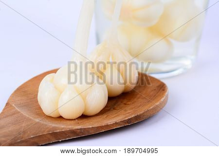 Pickled garlics on a wooden spatula. Pickled garlics in its preserved juice in a bottle as a background.  White background.