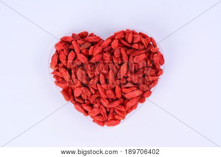 Dried Goji berries in a heart shape container with a white background.