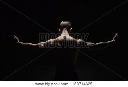 Unrecognizable man bodybuilder shows strong hands and neck muscles, athletic trapezius. Low key, studio shot on black background.