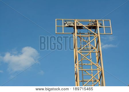 Yellow spotlight pole of outdoor stadium and blue sky clouds.