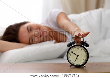 Sleepy young woman stretching hand to ringing alarm willing turn it off. Early wake up, not getting enough sleep, getting work concept