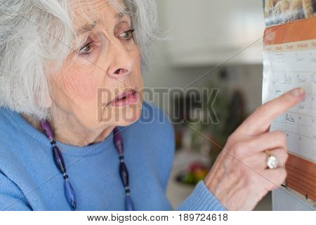 Confused Senior Woman With Dementia Looking At Wall Calendar