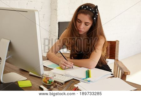 Portrait of young professional PR Manager female creating concept of promoting new services to market fitness apps. Attractive young woman looking at documents writing something. Creative work concept