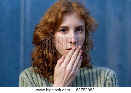 A Red-haired, Curly-haired Girl In A Green Pullover Frightened Her Hand Over Her Mouth. She Is Surpr